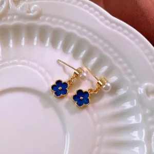 Elegant gold flower earrings with blue enamel petals and white pearl accent on white ceramic