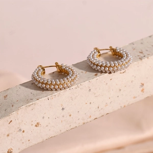 Macro detail of gold plated C-shape hoop earrings encrusted with small white pearls