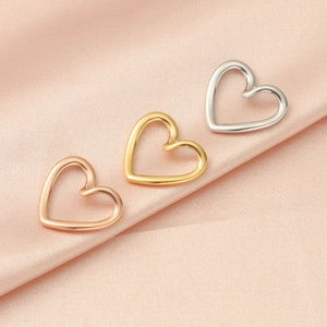 Hollow heart stainless steel pendants in gold, rose gold, and silver on pink silk fabric