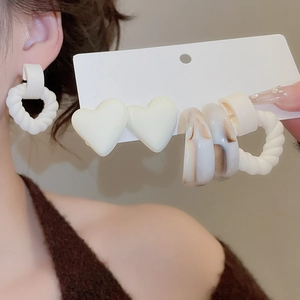 Detail of C-shaped acrylic earrings set with marble pattern and white heart charms