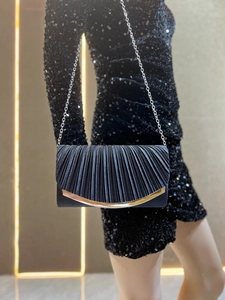 Detail of black pleated evening clutch with gold metal trim and silver chain strap