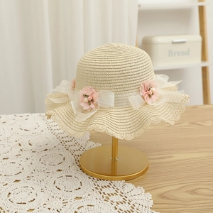 Détail du chapeau de paille avec fleur en soie rose et nœud en tulle sur le bord