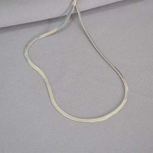 Detailed view of a sleek silver flat snake bone chain laid on soft textured fabric