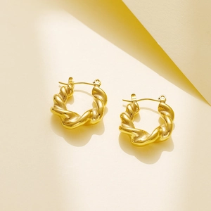 Detail of golden twisted rope earrings with high-shine metallic texture on beige background