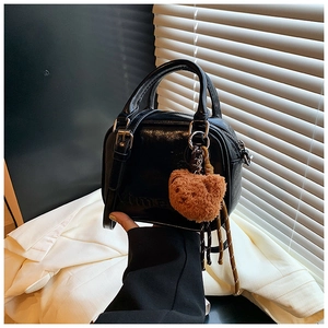 Detail of glossy black leather mini handbag featuring Vime embossing and a plush bear charm