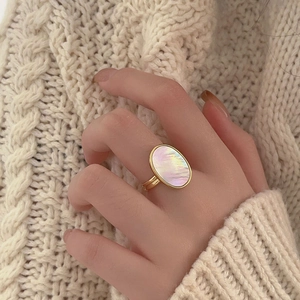 Close-up of a gold oval shell ring worn with a warm beige cable knit sweater