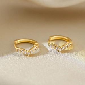 Detailed close-up of V-shaped gold earrings with white zircon on silk background
