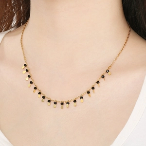 Golden choker necklace featuring black beads and teardrop pendants on model