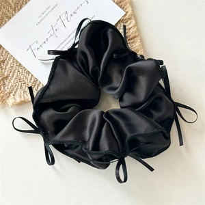 Close-up of black satin scrunchie with multiple ribbons on a woven table mat