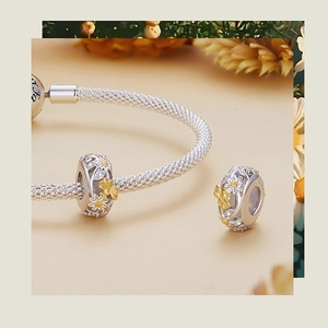 Detail of 925 silver daisy and bee charms with gold accents on a mesh bracelet