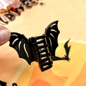 Creative black bat hair claw clip held in hand for festive Halloween styling