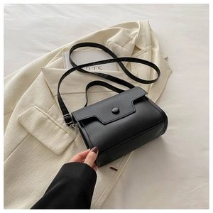 Close-up of black lychee grain leather crossbody bag styled on an ivory blazer