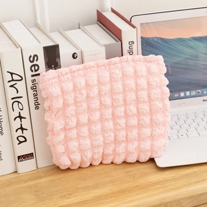 Neceser rosa de tela burbuja sobre escritorio de madera con portátil y libros al fondo