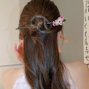 Detailed view of an ornate wooden hairpin with pink flowers and red tassels in a hair bun
