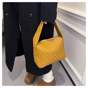 Close-up of a yellow studded shoulder bag in leather with silver rivets and zipper