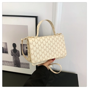 Detail view of cream white crossbody bag with brown M pattern on a black surface