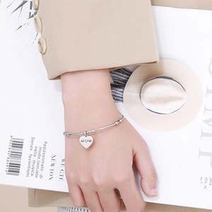 Bracelet jonjon argenté avec pendentif cœur gravé MOM sur un fond lifestyle élégant