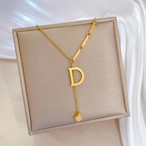 Minimalist gold necklace featuring letter D pendant and geometric cube on a silk backdrop