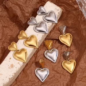 Double heart drop earrings in 18K gold and silver tones on minimalist background