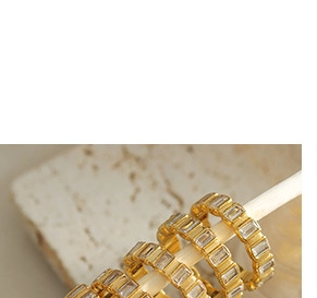 Détail macro de bagues dorées avec zircons taille baguette sur des supports blancs