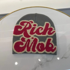 Close-up of gray knit beanie with red and beige Rich Mob lettering on marble surface