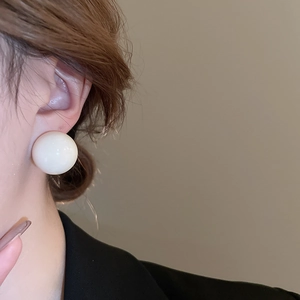Close-up of a large cream ball stud earring worn by a model with a clean minimalist style