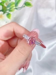 Detailed view of an oval pink gemstone ring on a hand with soft white silk background