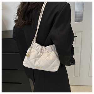 Detailed view of white quilted bucket bag with gold chain and metal sphere charm decoration