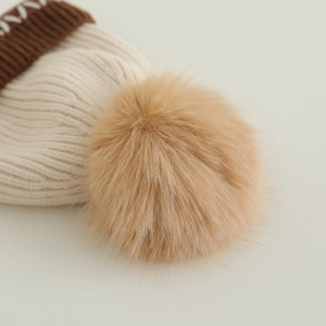 Detail der Strickmütze mit cremefarbener Textur, braunem Aufschlag und Kunstfell-Bommel