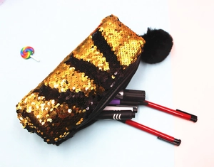 Detail view of double-sided gold and black sequin pencil case with plush ball charm