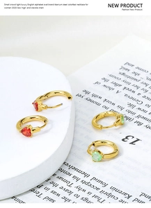 Macro detail of heart-shaped zircon earrings in red and mint green on golden titanium steel