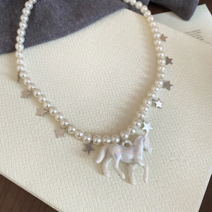 Détail d'un collier de perles avec un pendentif licorne irisé et des breloques étoiles
