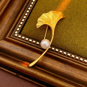 Gold plated ginkgo leaf brooch with pearl accent on luxury olive green fabric background