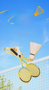 Détail d'un porte-clés badminton doré avec deux raquettes et un pendentif de volant blanc