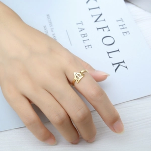 Close-up of golden Deathly Hallows symbol ring worn by a model in a minimal setting