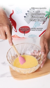 Detail of pink silicone spatula with wooden handle mixing eggs in a glass bowl