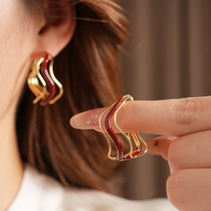 Close-up of wavy gold earrings with dark red enamel inlay on a model's ear