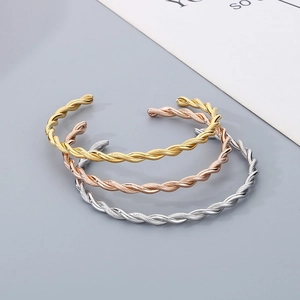 Detailed view of twisted cable texture on three metal cuffs in gold, silver and rose gold