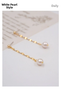 Detailed view of long gold tassel earrings with white pearls on vintage script background