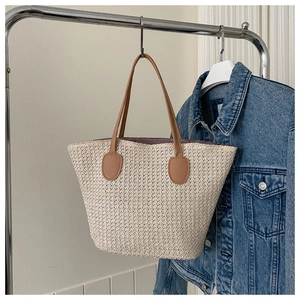 Detail of woven straw tote bag with brown leather handles and textured ivory finish