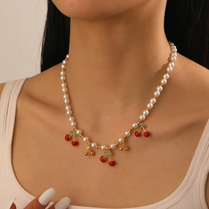 Détail macro du collier de perles avec pendentifs cerises rouges sur le cou