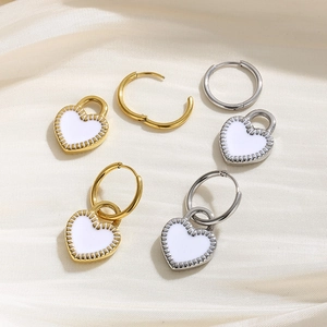 Close-up of heart earrings with white enamel center and serrated metal edges on silk