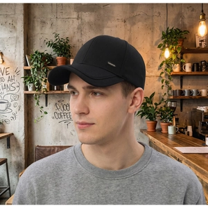 Detail einer schwarzen Baseballkappe mit Metalllogo an der Seite am Model im Café
