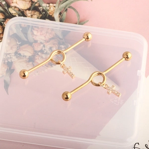 Detailed macro view of golden nipple rings featuring a twisted design and cross pendant