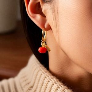 Detail of elegant gold hoop earring featuring red enamel persimmon and peanut charms
