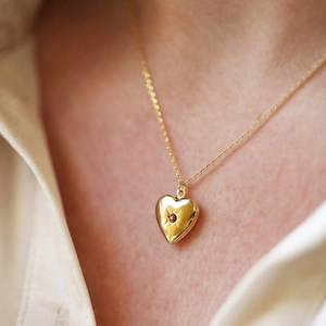 Golden heart locket necklace with red birthstone and sunburst engraving on a model