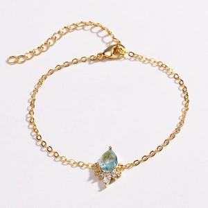 Detailed view of a gold chain bracelet with a blue water-drop gem and white zircons