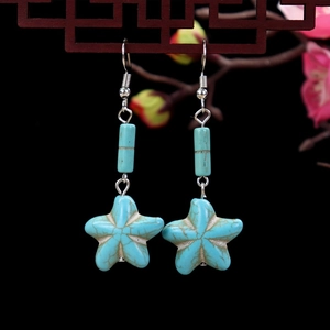 Star-shaped turquoise stone drop earrings with vintage silver hooks on dark wood background