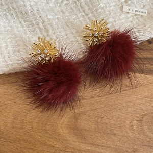 Close-up of burgundy fur ball earrings with golden firework rhinestone studs on wood