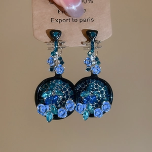 Dettaglio macro di orecchini a fiore in smalto blu con strass e ago d'argento